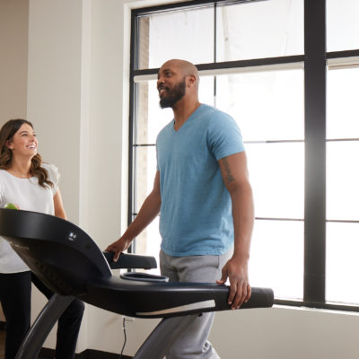 fit man walking on a treadmill with his female physical therapist next to him