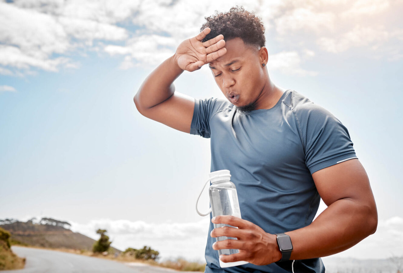 athletic man appearing exhausted and dehydrated from the heat wiping sweat from forehead